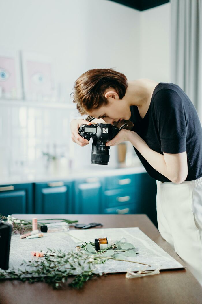 Woman using a DSLR camera to photograph items on a table, illustrating creativity escaping corporate hell tricks.