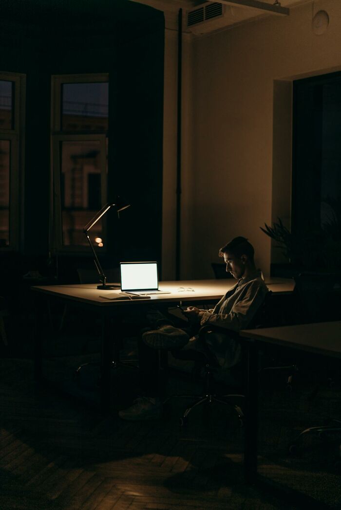 Person sitting alone in a dimly lit room at night, illuminated by a laptop screen, evoking a home alone horror atmosphere.