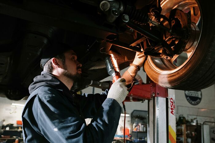 Mechanic inspecting car suspension with flashlight, illustrating subtle ways women have noticed misogyny in daily life.