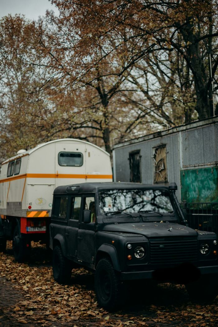 Black off-road vehicle parked near trailer and aging building in autumn forest, illustrating how dumb mistakes lead to consequences.