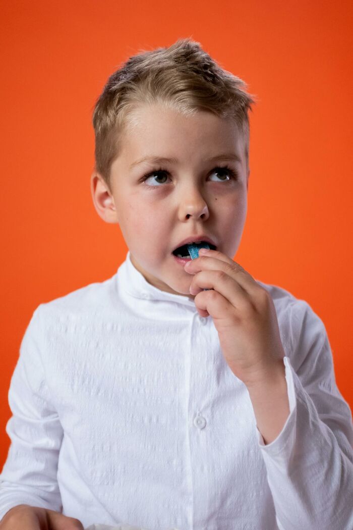 Young boy eating candy with a thoughtful expression against an orange background in a home alone setting.