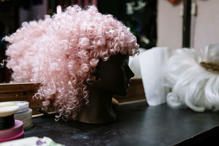 Curly pink wig on a mannequin head beside makeup products, evoking themes of nasty things exes did.
