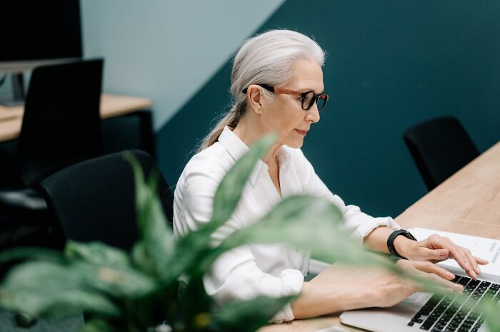 Older woman wearing glasses working on a laptop in an office, reflecting on moments of survival with no major injuries.