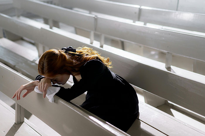Woman in black sitting alone on white bench, mourning loss, symbolizing siblings losing mom and HOA conflict over house.