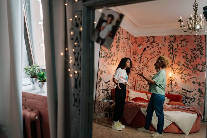 Two women arguing in a bedroom with floral wallpaper, conveying tension in a home alone setting that feels horrifying and scary.