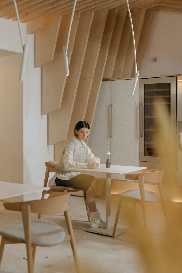 Woman sitting alone at a modern table in a minimalist cafe reflecting on things women are not allowed to do.