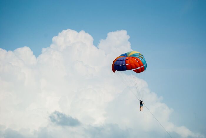 Person parasailing high in the sky with colorful parachute, showcasing a moment of survival with no major injuries.