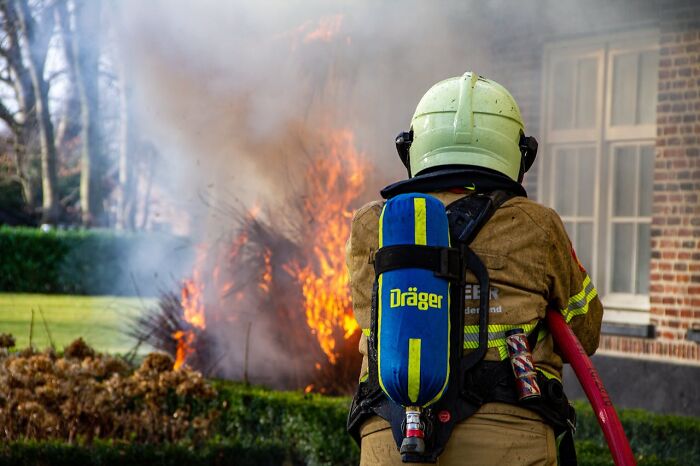 Firefighter in full gear battling a blazing fire outside a residential building during a terrifying moment of danger.