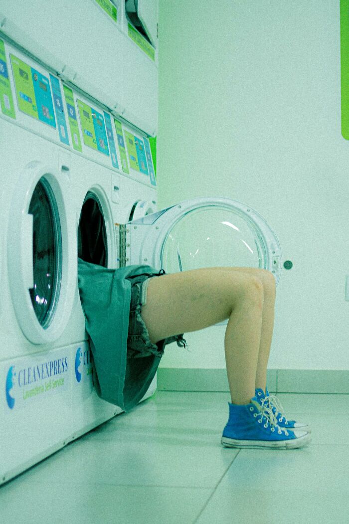 Person stuck halfway inside a washing machine in a laundromat, illustrating a very stupid very lucky terrifying moment.