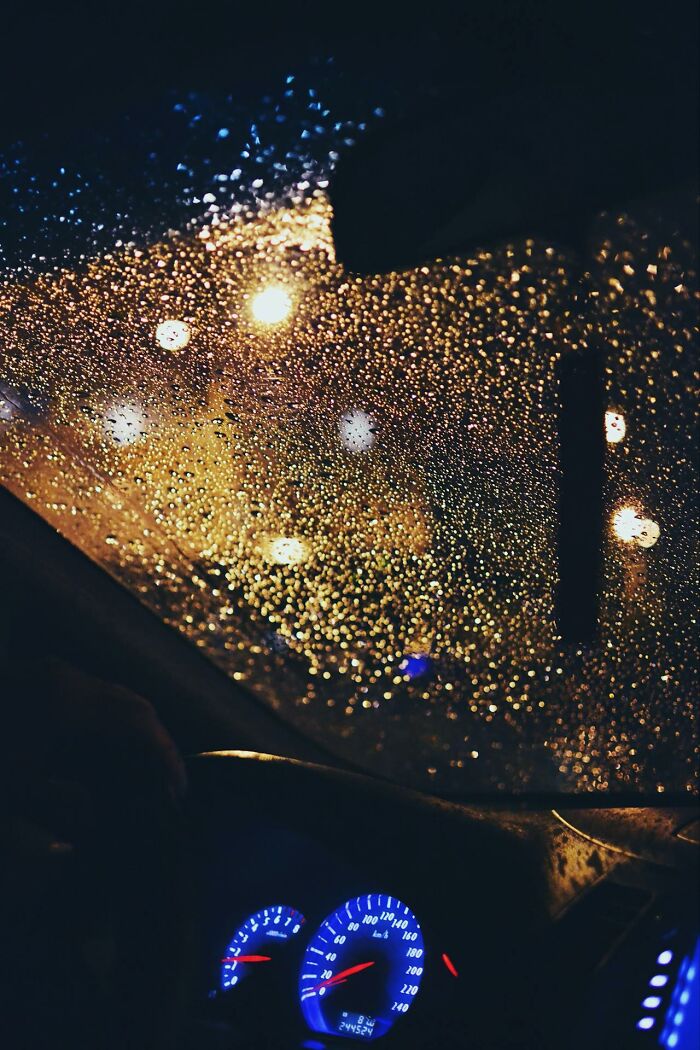 View through a rain-covered car windshield at night with illuminated speedometer, evoking moments of survival without major injuries.