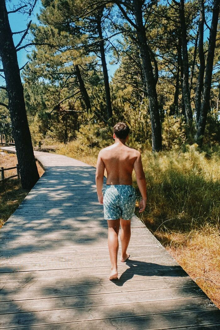A man walking barefoot on a wooden path through trees, illustrating things women are not allowed to do that men can.