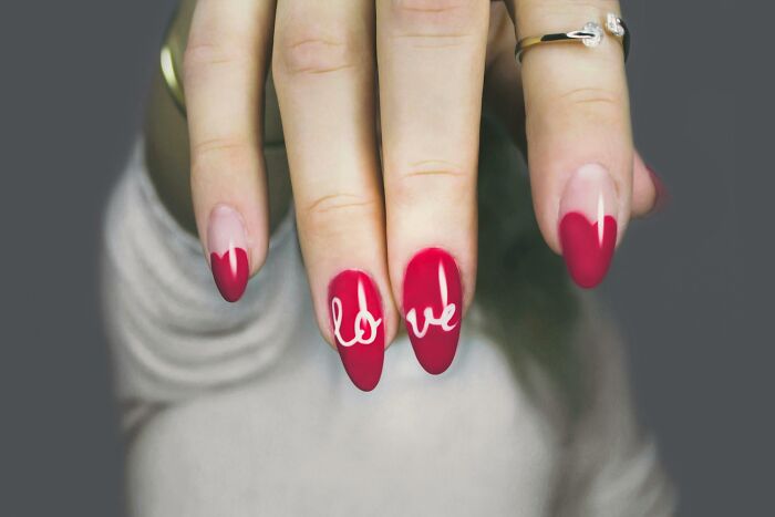 Close-up of hands with red nails and love design, people share sounds extremely angry expression implied by bold nail colors.