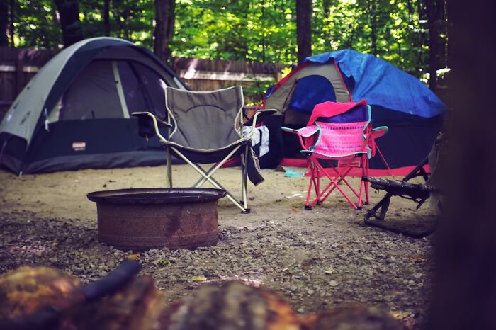 Empty camping chairs and tents at a quiet campsite in the woods, evoking the feeling of being alone and eerie forest encounters.
