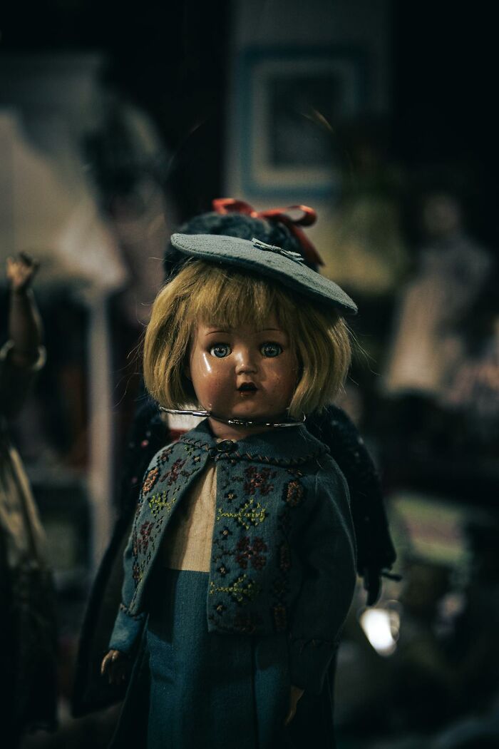 Antique doll with blonde hair and blue outfit in a dimly lit room, evoking a home alone horror atmosphere.