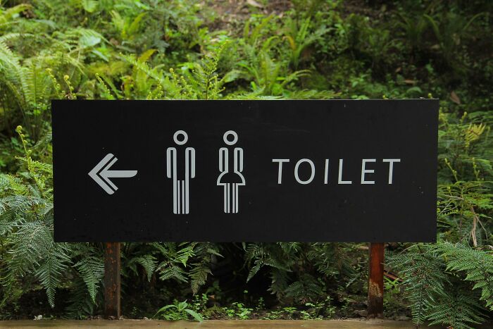 Toilet sign with male and female icons pointing left surrounded by green plants, illustrating a patient trying to fool doctors concept.