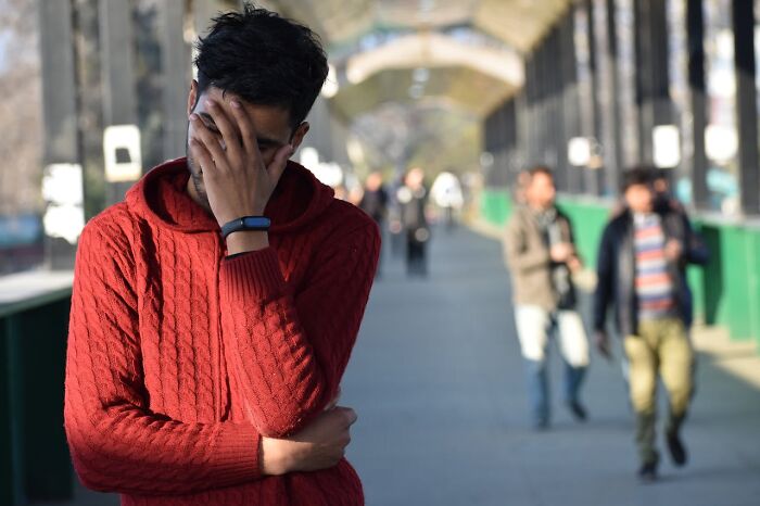 Man in red sweater covering face with hand, looking regretful, illustrating people who got fired due to dumb mistakes.