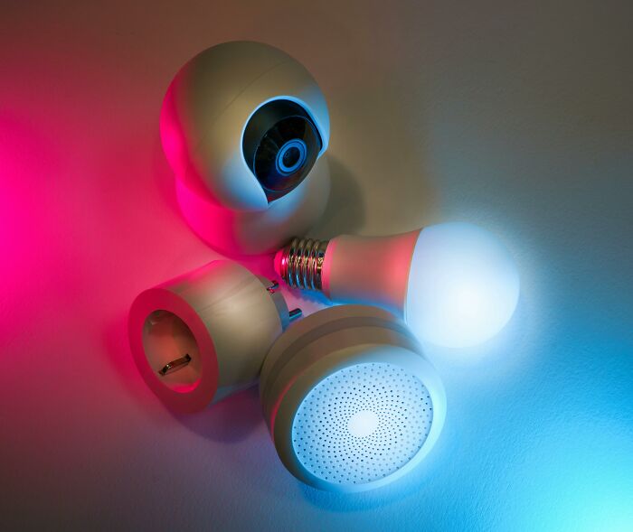 Smart home devices including security camera, light bulb, and smart plug shown with pink and blue lighting highlighting product sabotage examples.