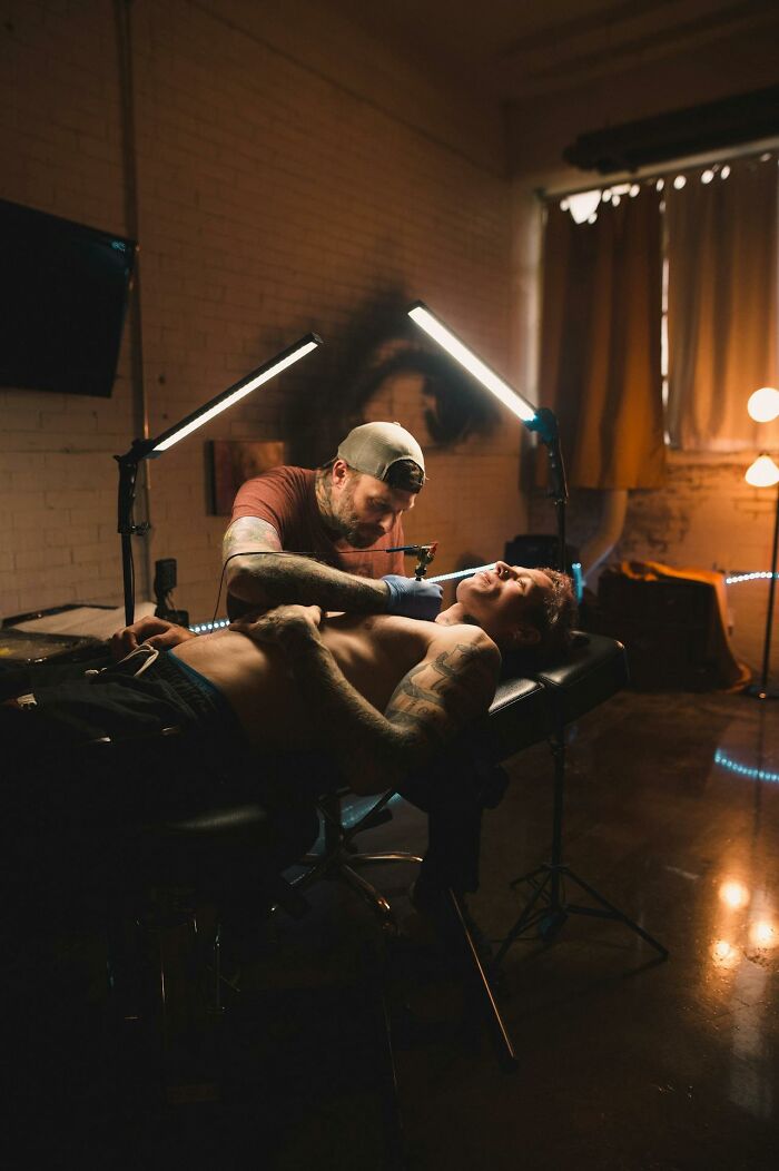 Tattoo artist focused on inking a client’s chest in a dimly lit studio with professional lighting setup.