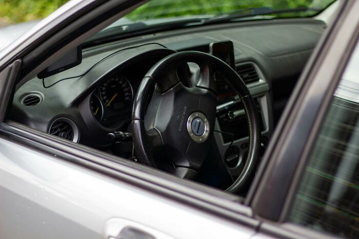 Steering wheel and dashboard of a parked car viewed through the open window, people share sounds extremely angry.