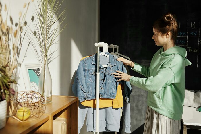 Young woman in green hoodie looking heartbroken while choosing clothes, symbolizing daughter heartbroken as parents watch TV all day.
