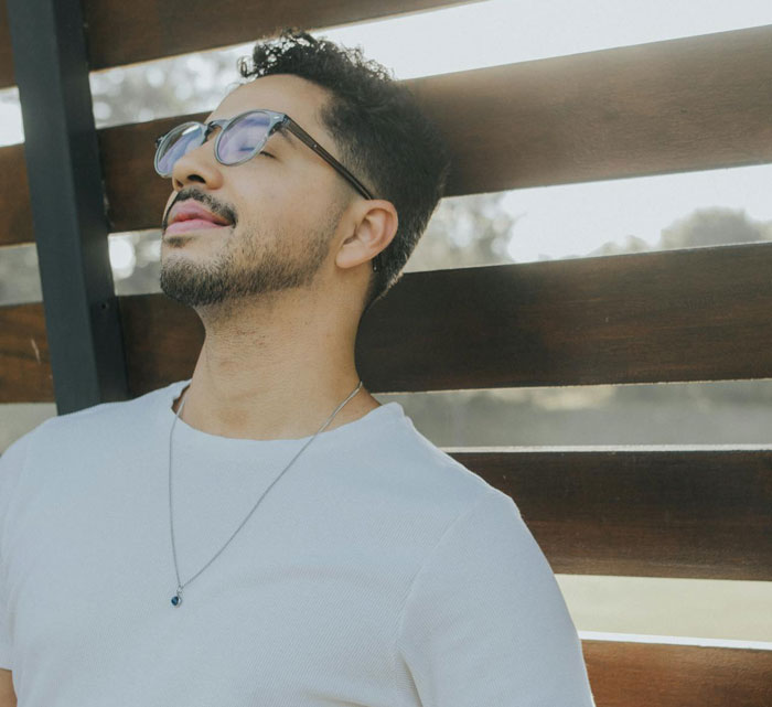 Man wearing sunglasses and a white shirt leaning against wooden fence in outdoor setting, adoption papers concept.