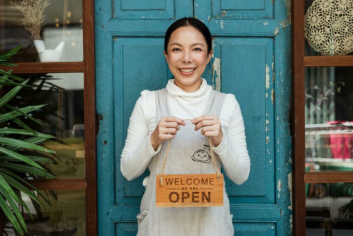 Smiling woman holding open sign, symbolizing real-life stories of people becoming what they once hated.