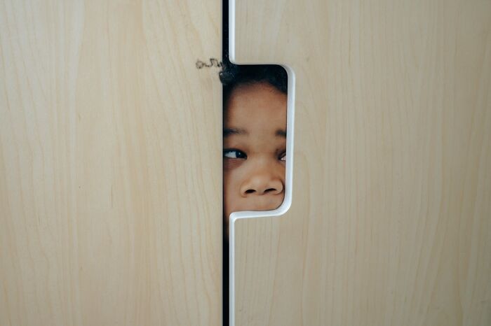 Child peeking fearfully through a narrow gap in a wooden door, capturing the feeling of home alone turning horrifying.