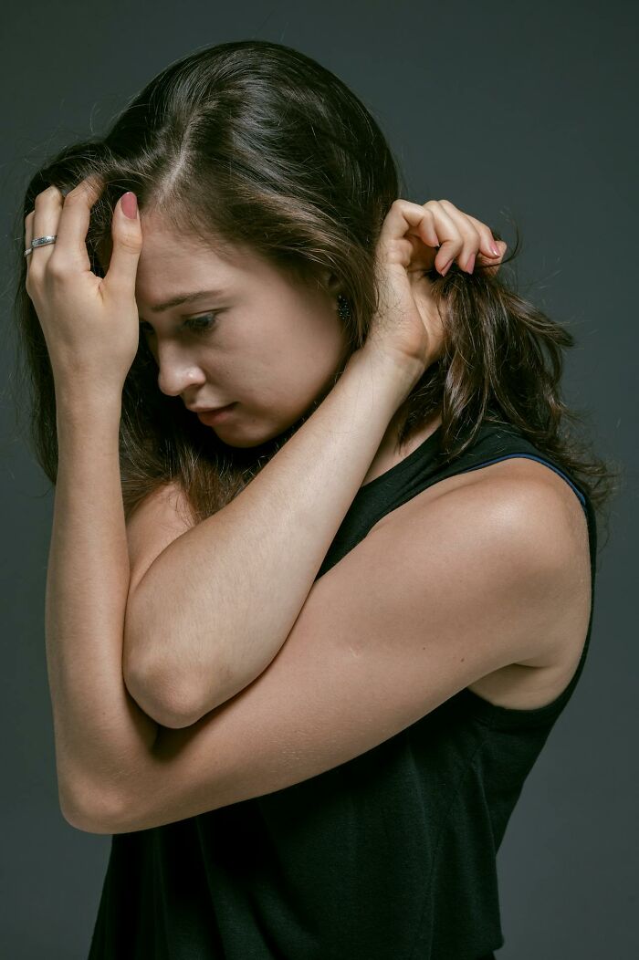 Young woman in black sleeveless top looking down, expressing emotion related to things women are not allowed to do.