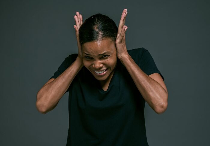 Person covering ears in fear, expressing discomfort from creepy things encountered alone in the woods.