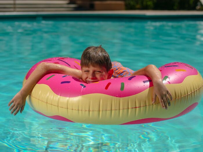 Boy floating on a pink donut pool float in clear water, capturing a lucky moment in a summer swimming pool.
