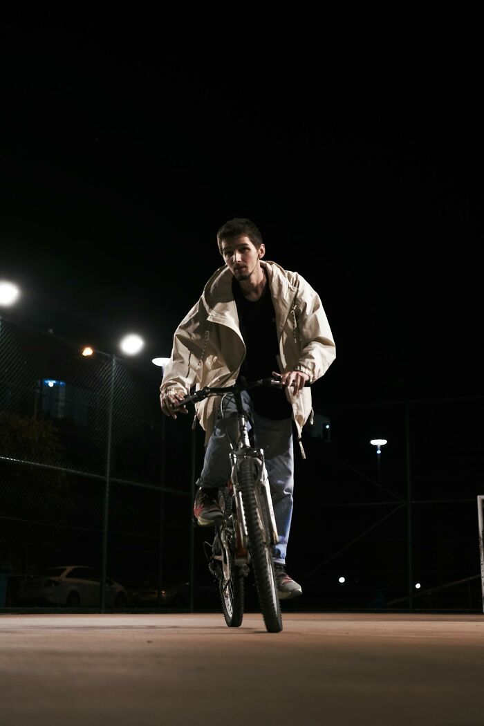 Young man riding a bicycle at night under bright lights, depicting a very stupid very lucky moment of risk and survival.