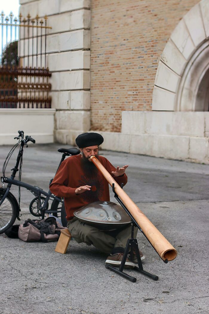 Man playing didgeridoo and handpan outdoors near a bicycle, illustrating things women are not allowed to do compared to men.