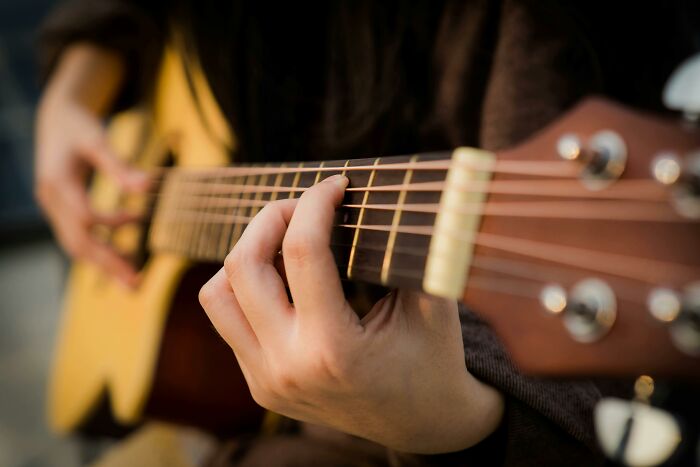 Close-up of hands playing acoustic guitar strings, highlighting the sweet facade of skill and emotion.