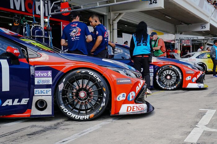 Race cars lined up in the pit lane with crew members attending, highlighting luxury jobs serving ultra-wealthy people.