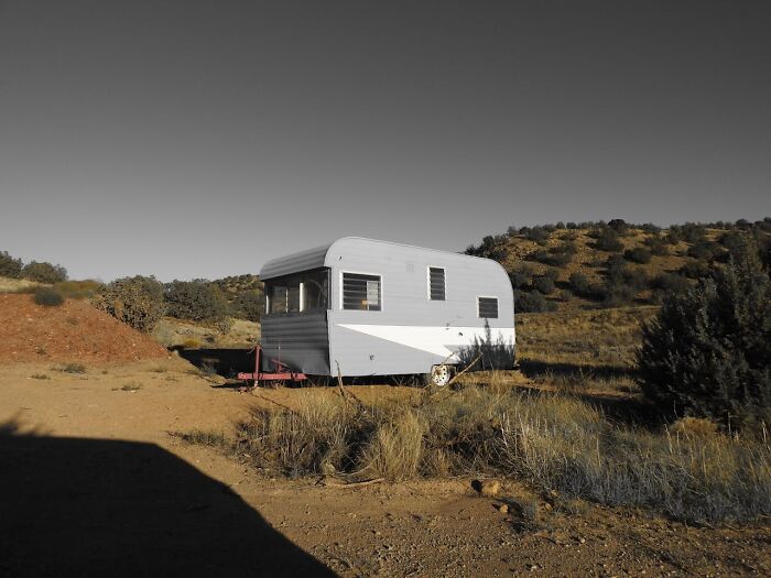 Small vintage trailer parked alone in the woods surrounded by dry grass and hills, evoking creepy encounters while alone.