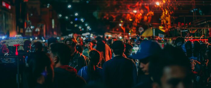 Crowded night market scene with people walking under streetlights, capturing the contrast of a sweet facade hiding manipulation.