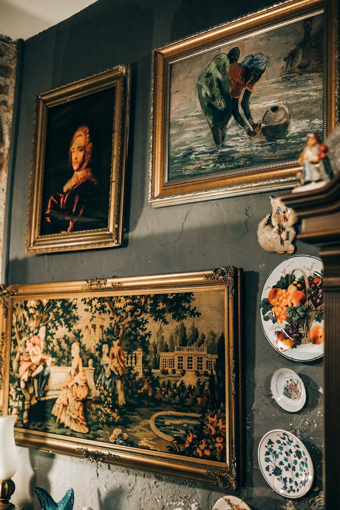 Vintage paintings and decorative plates on a dimly lit wall evoking creepy stories perfect to tell in dark woods.