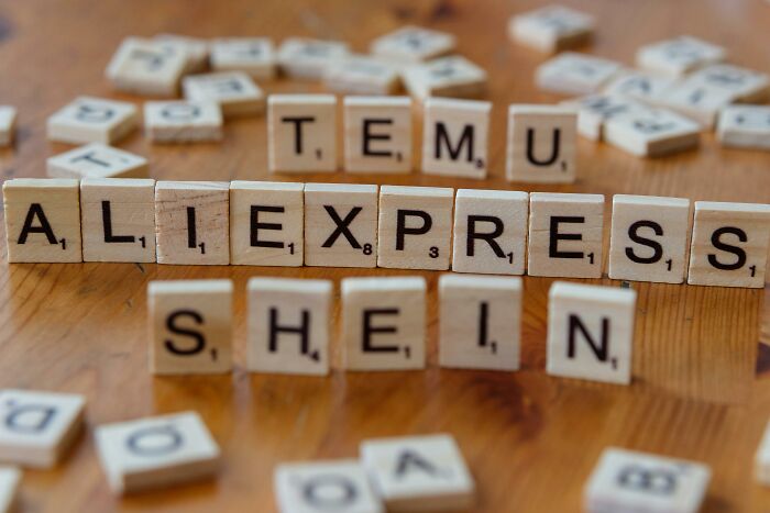 Scrabble tiles arranged to spell popular overhyped products like AliExpress and Shein on a wooden table.