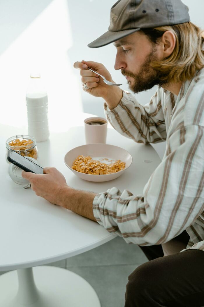 Man eating cereal while looking at smartphone, illustrating moments people got fired due to dumb mistakes.