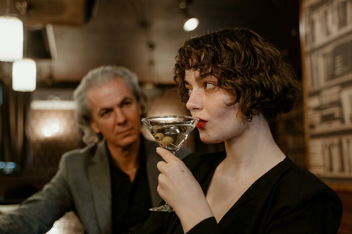 Woman drinking a cocktail while a man watches, illustrating the atmosphere of shocking family secrets revealed.