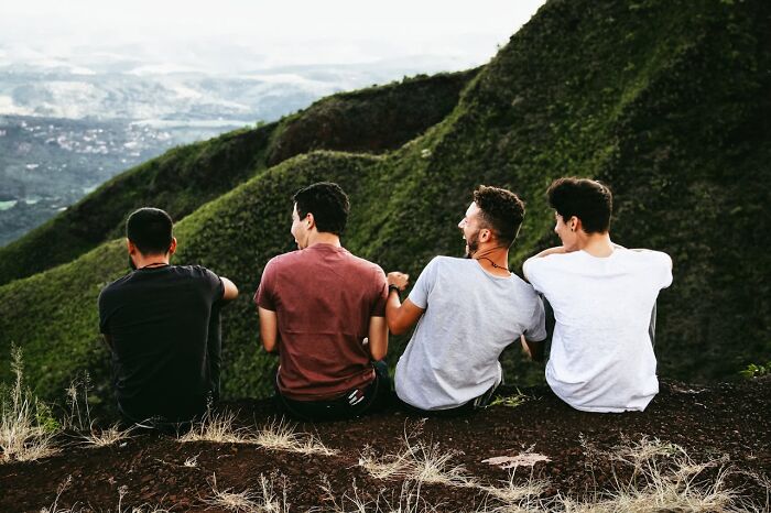 Four men sitting on a hillside overlooking green mountains, illustrating things women are not allowed to do that men can do freely.