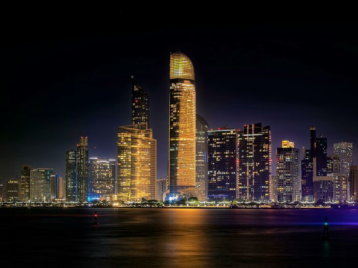 Night skyline of a city with illuminated skyscrapers reflecting on water, showcasing former capitals in a sneaky urban view.