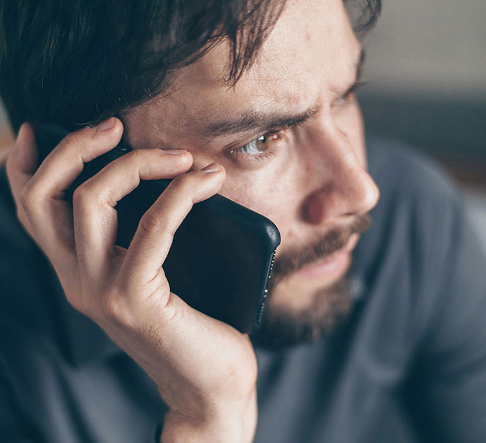 Young man looking troubled while talking on the phone, representing entitled lady manipulating boyfriend breakup situation.