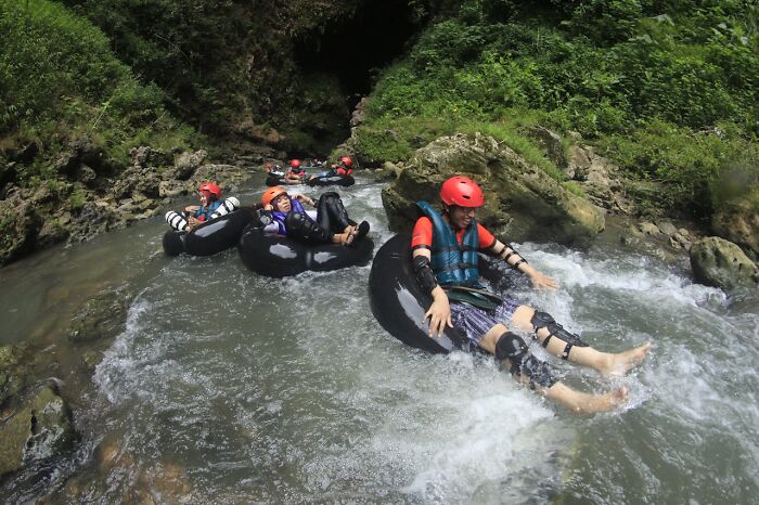 Group of people tubing down a river wearing helmets and life vests, capturing moments of surviving without major injuries.