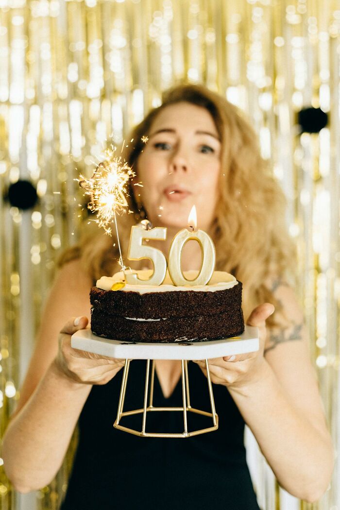 Woman celebrating with a birthday cake and sparklers, illustrating themes of things women are not allowed to do freely.
