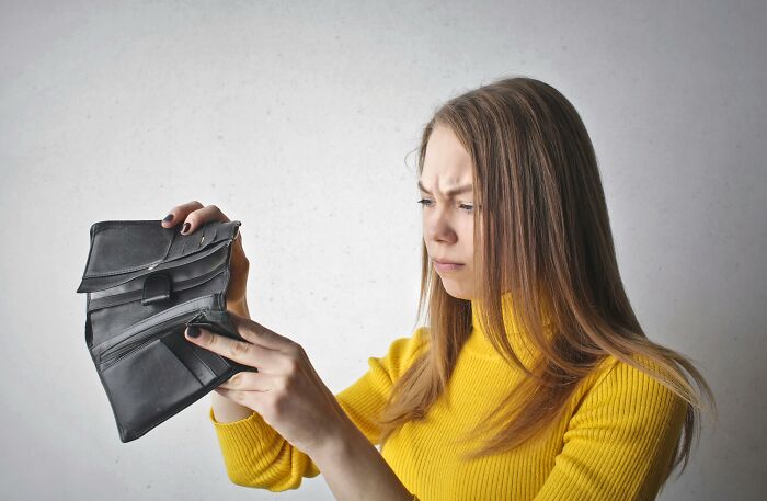 Young woman in yellow sweater looking confused at an empty wallet, evoking real-life hexes and odd curses concept.