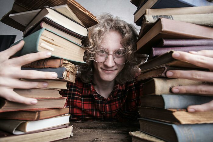 Young person with glasses and curly hair, surrounded by stacks of old books, ready for a trivia genius true-or-false quiz.