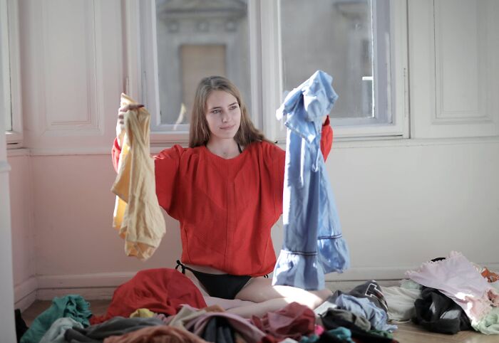 Woman sorting clothes in a sunlit room, surrounded by garments, highlighting things women are not allowed to do freely.