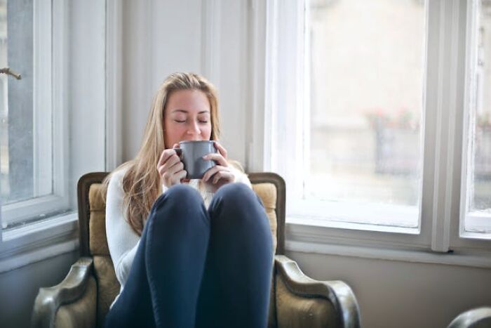 Woman sitting in a cozy chair by the window, enjoying a warm drink, surrounded by a calm and relaxed atmosphere.