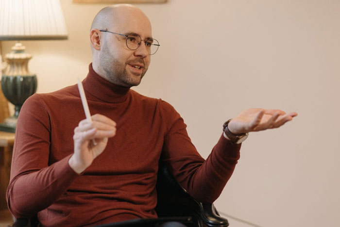 Man in glasses and a brown turtleneck explaining sister sending adoption papers after babysitting offer misunderstanding